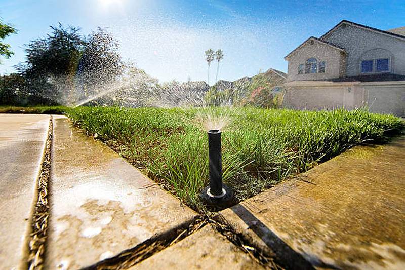 Pop-up sprinkler watering a lawn beside a pavement, Waterkloof